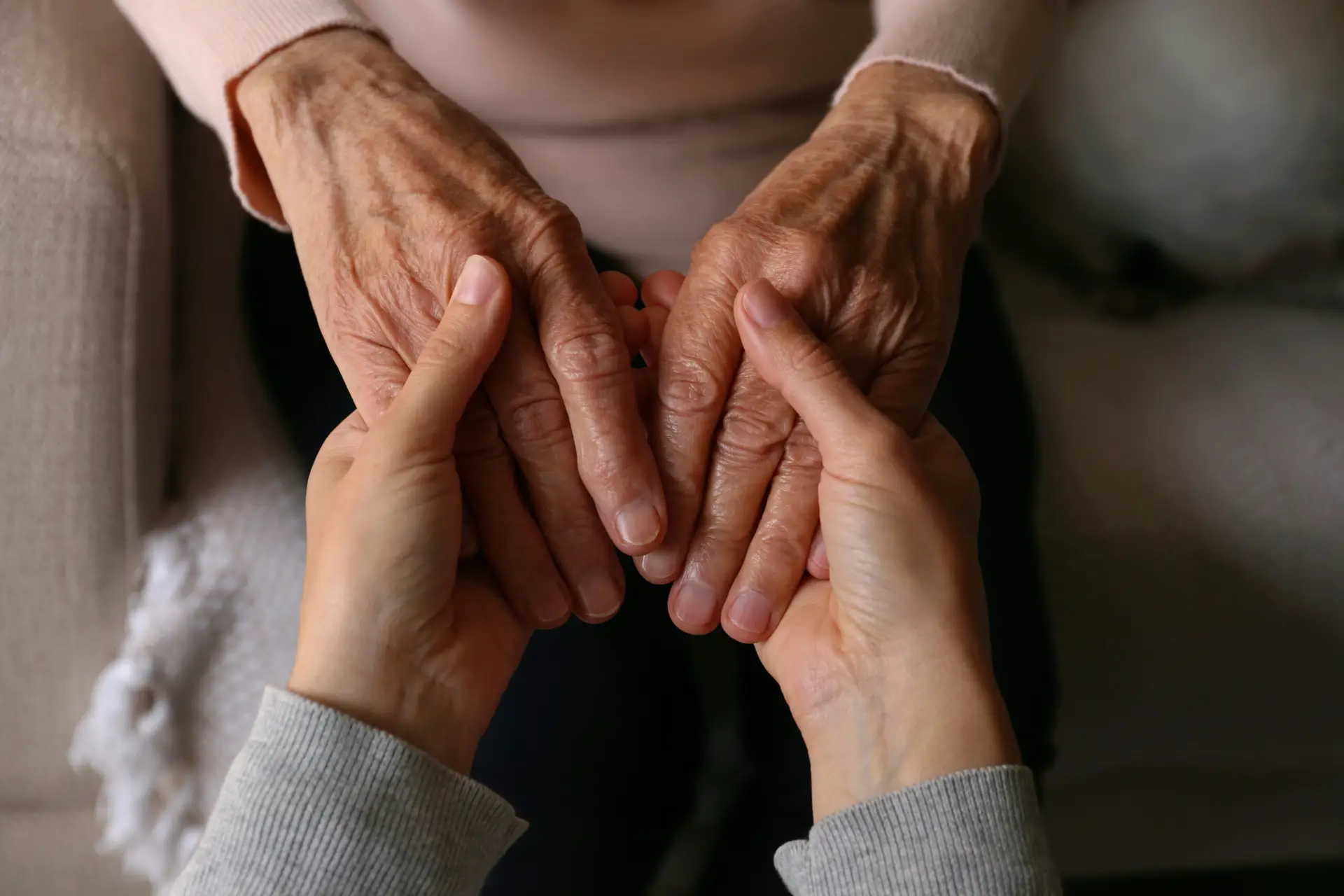 A younger person gently supporting the hands of an older adult