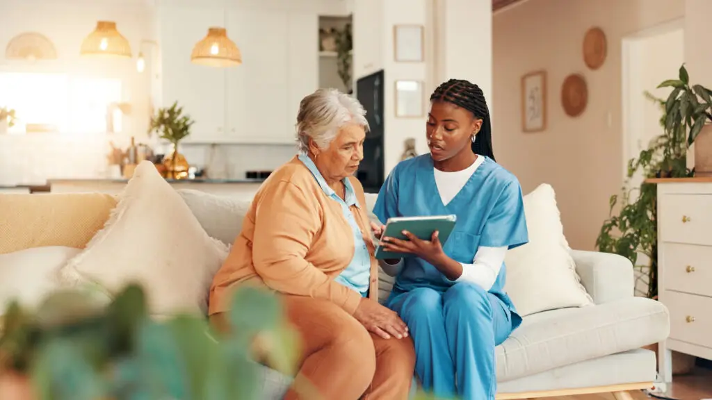 A home healthcare nurse and an older woman reviewing information on a tablet