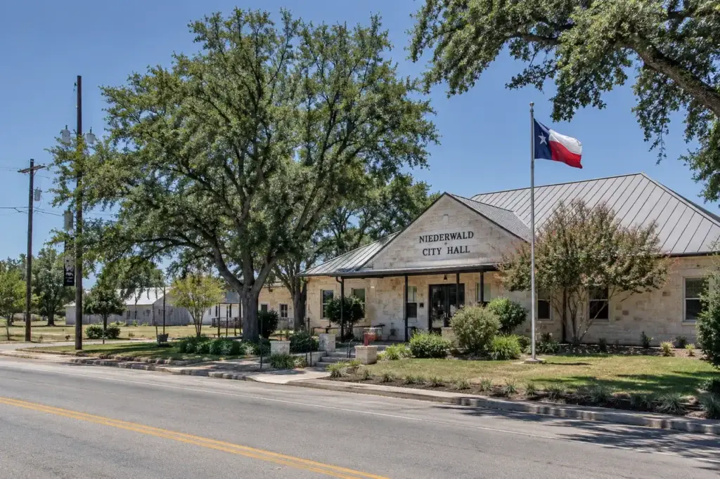 Niederwald City Hall in Niederwald, Texas with mature oak trees and Texas flag