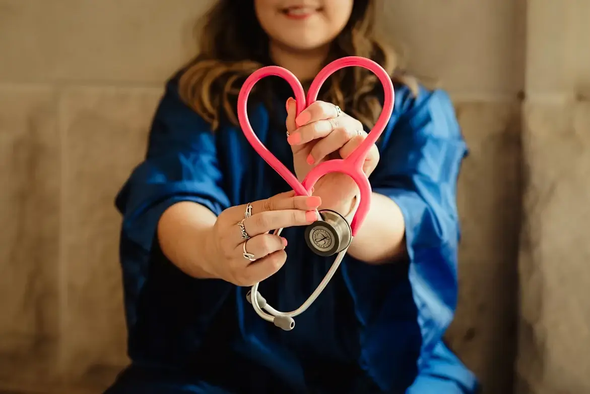 Woman in scrubs holding a stethoscope in a heart shape.